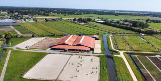 van manege met grote binnenhal, buitenrijbanen en weilanden met paarden aan de Amperestraat 8d in Hillegom.